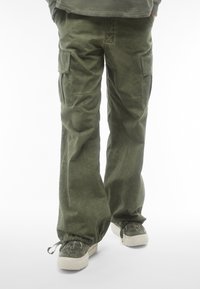 Pantaloni cargo di colore verde oliva, realizzati in tessuto testurizzato, presentano tasche laterali e una vestibilità rilassata. I polsini sono elasticizzati per una regolazione ottimale.