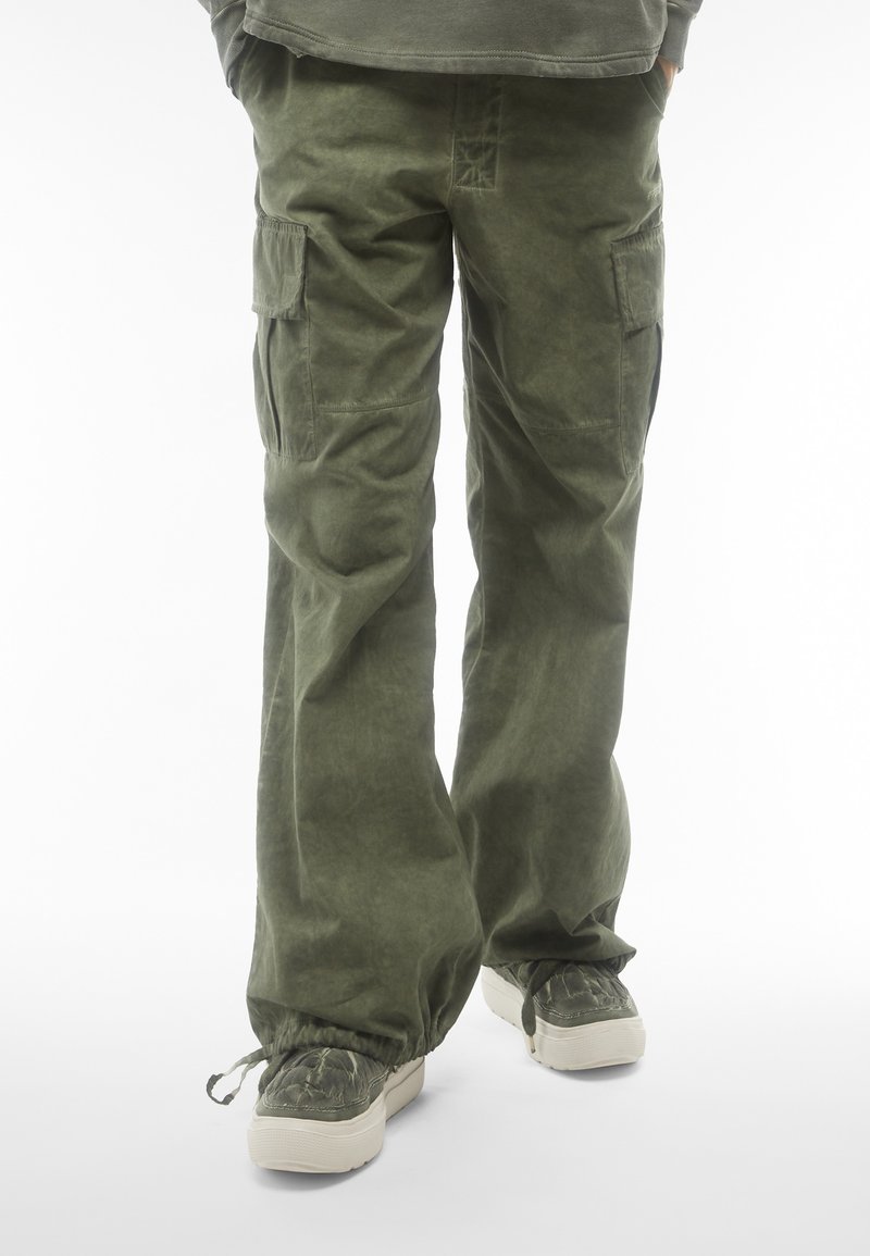 Pantaloni cargo di colore verde oliva, realizzati in tessuto testurizzato, presentano tasche laterali e una vestibilità rilassata. I polsini sono elasticizzati per una regolazione ottimale.