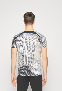 Short-sleeve jersey shirt in black, white, and beige with a geometric pattern. Features a rounded neckline and smooth, lightweight fabric.