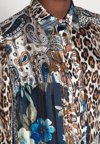 Col et haut de poitrine d'une chemise à motifs combinant imprimé léopard, floral, paisley et rayé dans des tons de bleu, marron, blanc et noir.