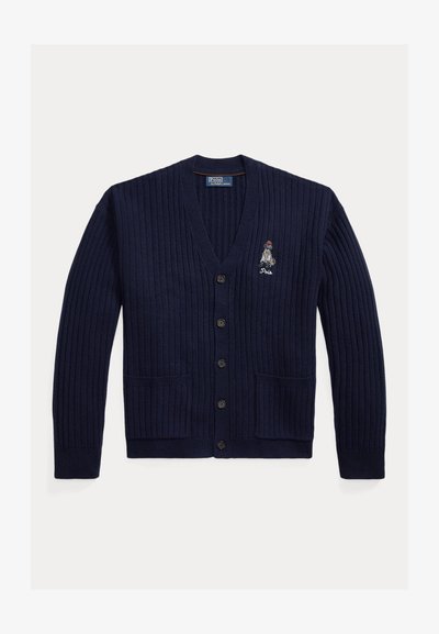 Cardigan bleumarin cu țesătură în relief, cu guler în V, șase butoane frontale și două buzunare frontale. Are un grafic brodat în partea superioară stângă.