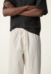 Camiseta de punto negra con mangas cortas; pantalones de rayas en color crema con cintura elástica. Superficie texturizada y rayas verticales.