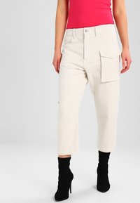 Beiga cargobyxor med sidoficka, smal passform och uppvikta avslut. I kombination med svarta ankelstövlar och en rosa topp. Mat yta.