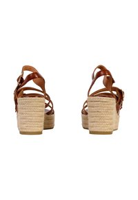 Sandales à talons compensés en cuir marron avec des brides entrecroisées, ayant un talon recouvert de jute texturé et une semelle lisse. Perspective de l'arrière.