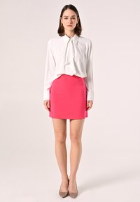 White long-sleeve blouse with a neck tie, paired with a fitted pink mini skirt and sparkly pointed-toe heels. Smooth texture throughout.