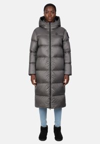 Lang grå pufferjakke med hætte, med en frontlynlås, firkantet form, quiltede sektioner og glat tekstur, båret over lyseblå jeans.
