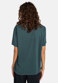 T-shirt in cotone verde acqua con maniche corte, vestibilità rilassata e orlo arrotondato. La parte posteriore presenta una texture liscia e non ha loghi o motivi visibili.