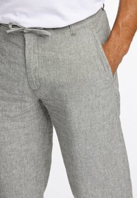 Pantalons en lin gris clair avec une taille élastique à cordon, des poches latérales et un tissu texturé pour la respirabilité et le confort.