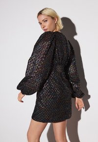 Zwarte jurk met een getextureerd, golvend patroon en een meerkleurige glans. Pofmouwen en een nauwsluitend silhouet zorgen voor opvallende designelementen.