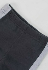 Pantalon en tissu gris foncé avec ceinture et bandes latérales gris clair, montrant un gros plan des coutures et de la ceinture élastique.