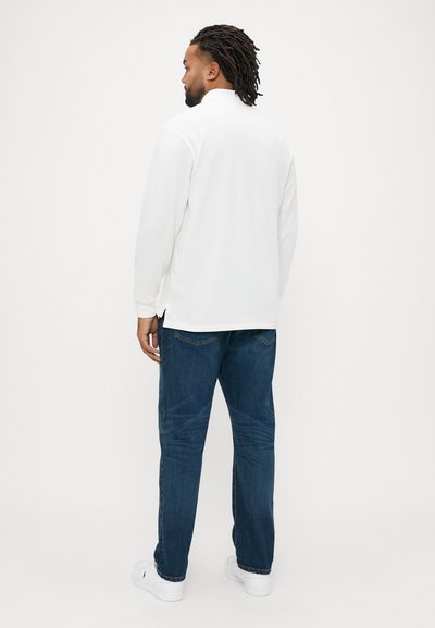 Άσπρο πουκάμισο με μακριά μανίκια και μικρό γιακά, συνδυασμένο με μπλε τζιν. Το σύνολο έχει άνετη εφαρμογή και καθαρό, απλό σχεδιασμό.