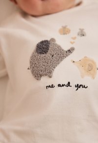 Camiseta blanca de algodón con bordado de elefante gris y cerdo beige, con pequeños corazones y texto "yo y tú" en negro debajo.