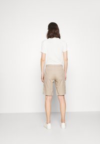 Beige Shorts aus glattem Stoff, knielang mit lockerem Sitz, mit Gesäßtaschen und einem Bund, kombiniert mit einem weißen T-Shirt.