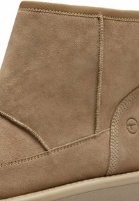 Beige semskede ankelstøvler har en glatt tekstur, sydd detaljer og elastiske aksenter på toppen. Rund tå, minimalistisk design.
