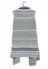 Indumento senza maniche con motivo in nero, bianco e blu. Presenta un design a zigzag e un orlo irregolare. Il tessuto sembra testurizzato e leggero.