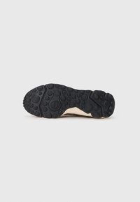 Suela de goma negra con patrones circulares y un mediopié color crema. El diseño promueve la tracción y estabilidad en diversas superficies.
