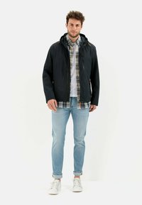 Black, lightweight jacket with a hood and zippers, worn over a checkered shirt, paired with light blue jeans and white sneakers.