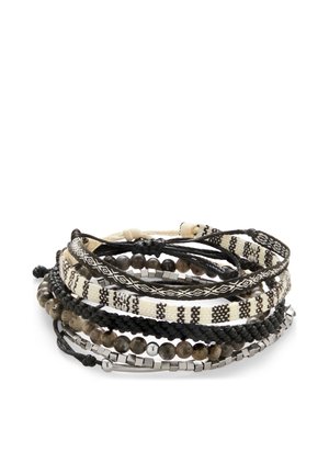 Stak af sorte, hvide og grå armbånd, herunder flettede, perlebesatte, mønstrede stof- og metalterningdesigns på en hvid baggrund.