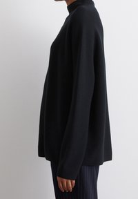Pull à col roulé noir avec une coupe ample et décontractée. Confectionné dans un tissu tricoté texturé, doté de manches longues et d'un design minimaliste.
