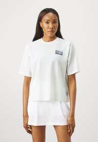 Αθλητικό μπλουζάκι κοντό μανίκι ανοιχτό πράσινου διχτυού με στρογγυλή λαιμόκοψη και μπλε λογότυπο. Συνδυάζετα�ι με άσπρη πλισέ φούστα.