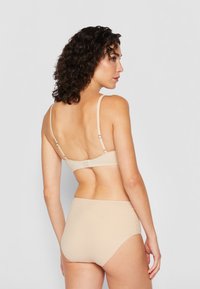 Beige seamless bra and high-rise brief, featuring thin adjustable straps and a stitched back closure for secure fit. Smooth, matte texture.