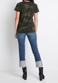 Grön camouflagemönstrad t-shirt med korta ärmar, kombinerad med ljusblå jeans med upprullade ben och svarta högklackade ankelboots.