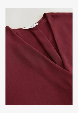 Bordowa bluzka o gładkiej fakturze, z dekoltem w serek, złożonymi fałdami z przodu oraz metką na wewnętrznej części kołnierza.