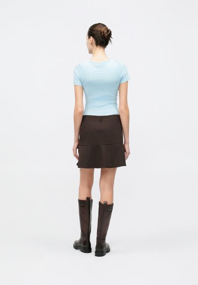 Haut ajusté à manches courtes bleu clair, jupe évasée marron avec design en couches, et bottes hautes en cuir marron à finition mate.