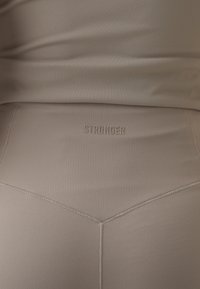 Beige prestasjonsleggings med teksturert finish, med sømdesign og embossert "STRONGER"-logo på midjen.