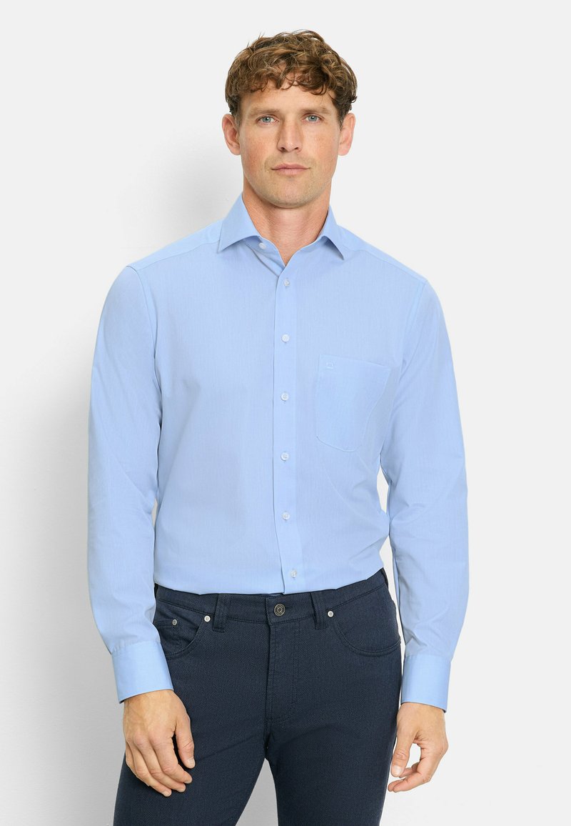 Camicia azzurro chiaro a maniche lunghe con taschino, texture liscia e colletto classico, abbinata a pantaloni scuri.