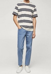 Camicia a maniche corte a righe nei colori blu navy e crema, abbinata a jeans dritti azzurri chiari e sneakers bianche. Tessuti a trama liscia.