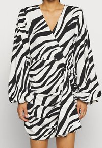 Robe à imprimé zèbre noir et blanc avec manches longues, col en V, taille froncée et tissu texturé. Silhouette drapée avec des détails froncés.