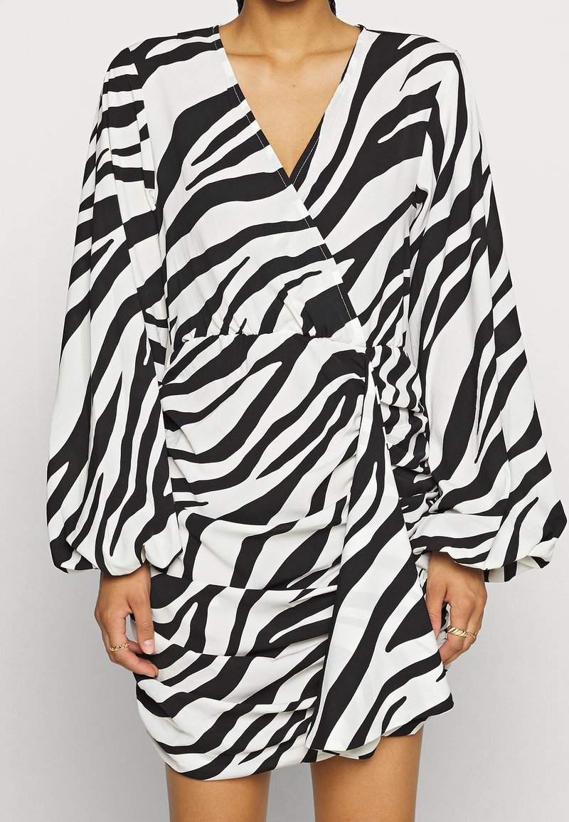 Robe à imprimé zèbre noir et blanc avec manches longues, col en V, taille froncée et tissu texturé. Silhouette drapée avec des détails froncés.
