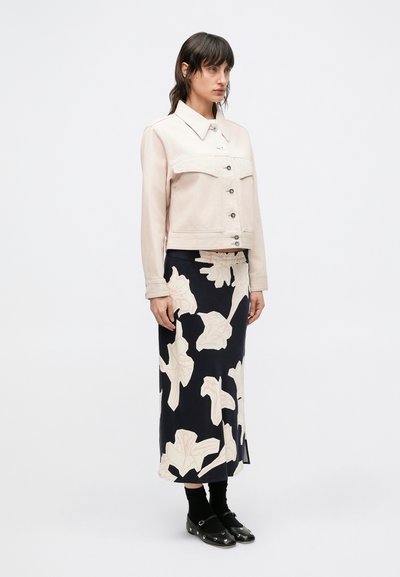 Ροζ ανοιχτόχρωμο τζιν μπουφάν με γιακά και μπροστινές τσέπες, σε συνδυασμό με φούστα ναυτικού μπλε με μεγάλο λουλουδάτο σχέδιο σε λευκό χρώμα. Μαύρα παπούτσια.