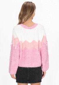 Lekki, dziany sweter z białą górną częścią, różowym wzorem w zygzak oraz miękkim, teksturowanym wykończeniem. Długie rękawy z dekoracyjnymi akcentami.