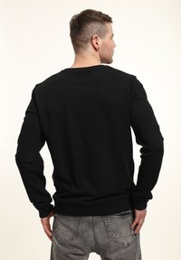 Sudadera negra de manga larga con cuello redondo y puños y dobladillo de canalé, confeccionada en una tela suave, mostrada desde la vista trasera.