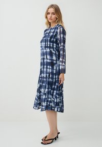 Granatowa sukienka midi tie-dye z długimi rękawami, okrągłym dekoltem, plisowaną spódnicą i czarnymi sandałami na obcasie. Gładki, lekki materiał.