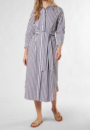 Femme portant une robe midi à rayures verticales bleues et blanches, boutonnée, manches longues, une ceinture assortie à la taille et des sandales slides beiges.