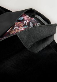 Zwarte fluwelen jack met een glanzende revers. De binnenkant heeft een bloemenpatroon in bordeaux, crèmekleur en blauw op een donkere achtergrond.