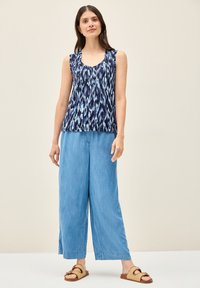 Ärmelloses marineblaues Oberteil mit einem hellblauen abstrakten Muster, kombiniert mit weiten hellblauen Hosen und braunen Riemchensandalen.