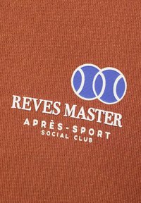 Tessuto a maglia marrone con testo bianco "REVES MASTER APRES-SPORT SOCIAL CLUB" e due grafiche di palline da tennis blu sopra il testo.