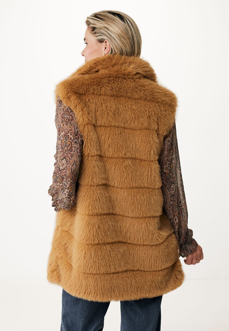 Chaleco de piel sintética en un cálido color marrón dorado, con un cuello alto y un diseño de acolchado horizontal. Blusa de manga larga estampada visible.