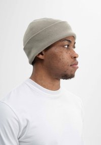 Graue gerippte Mütze, die auf einem Kopf getragen wird, ergänzt durch ein schlichtes weißes Rundhals-T-Shirt. Weicher Textur sichtbar mit enger Passform.