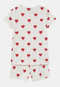 Completo pigiama per bambini in morbido cotone bianco, con un motivo ripetuto di cuori rossi sia sulla maglietta che sui pantaloni.
