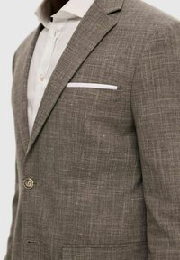 Blazer en lin gris mélangé avec tissu texturé, fermeture à un bouton et poche poitrine avec accent de mouchoir blanc.