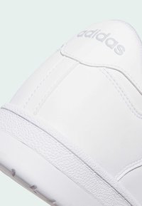 Biele tenisky s hladkým syntetickým zvrškom, textúrovanou gumovou podrážkou, viditeľným prešitím a embosovaným logom na päte.