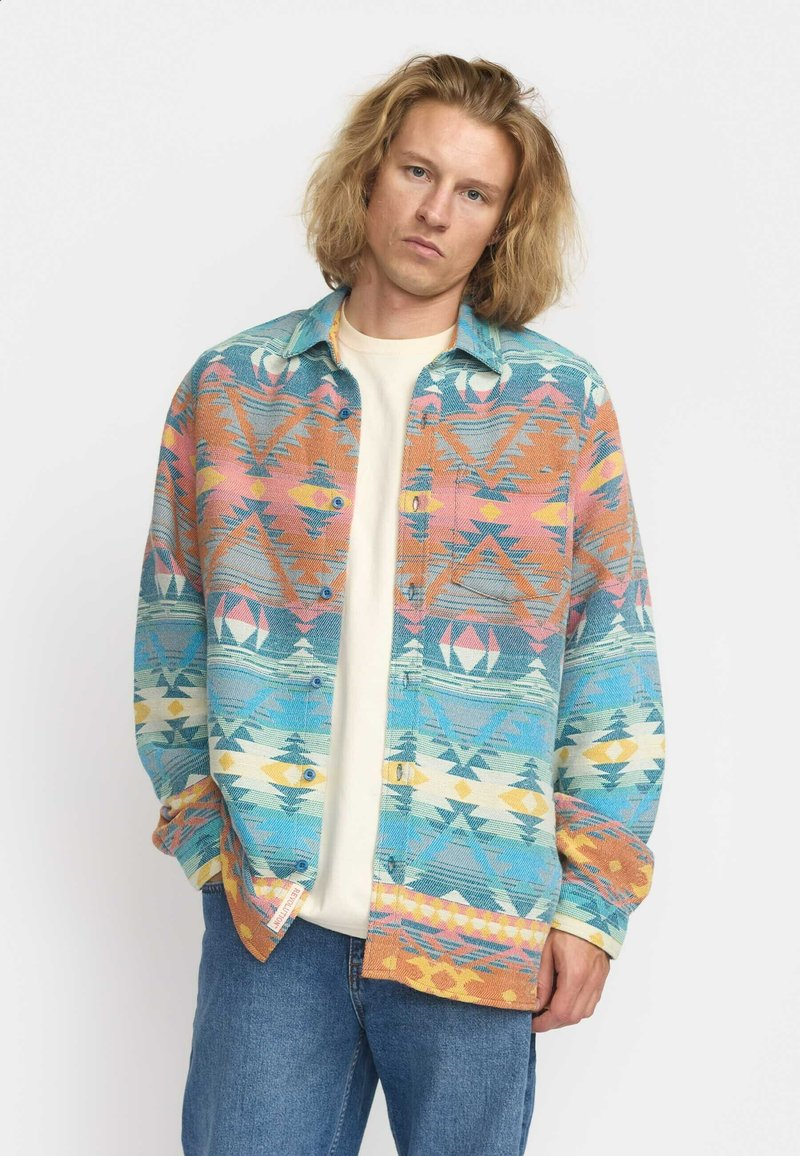 Geweven blouse met lange mouwen, voorzien van een kleurrijk geometrisch patroon in hoofdzaak turquoise, oranje en roze, met een zachte textuur.