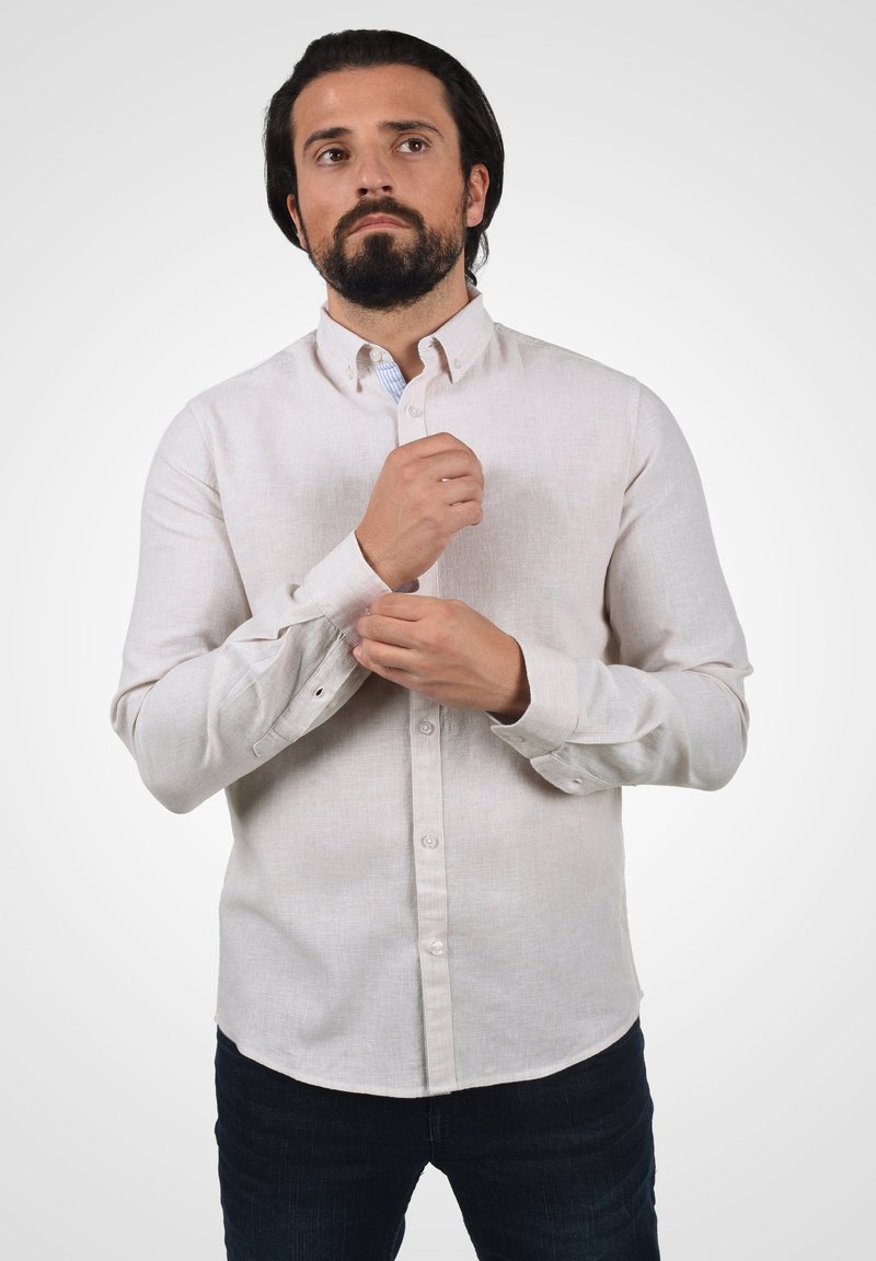 Lys beige skjorte med knapper lavet af struktureret stof, med lange ærmer, krave og knappede manchetter, båret med mørke denimjeans.