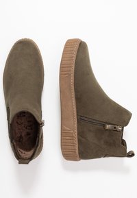 Olivgröna ankelstövlar i mocka med sidodragkedja, strukturerad brun gummisula och mjukt innertyg.