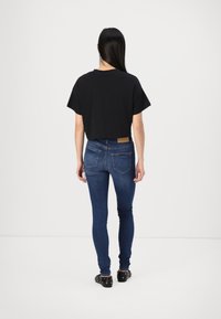 Svart kortärmad t-shirt i croppade modellen, matchad med mörkblå slim-fit jeans som har diskret detaljer på bakfickorna och en brun läderlabel.